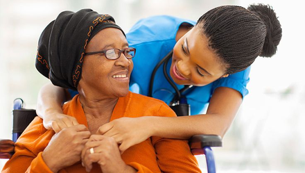 A nurse smiling with an older patient in a wheelchair